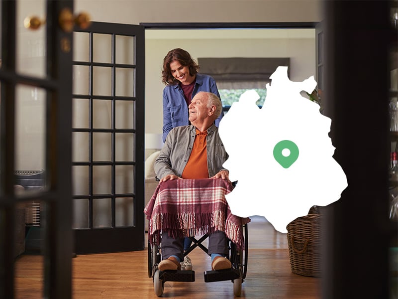 Angehörige schiebt älteren Mann im Rollstuhl durch die Wohnung