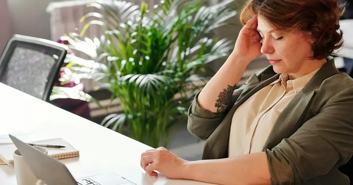 Nachdenkliche Frau im Büro mit geschlossenen Augen und Hand an der Stirn – Symbolbild für psychische Gesundheit und Stressbewältigung im Alltag.